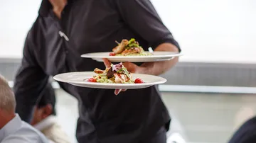 A waiter carries two plates of food.