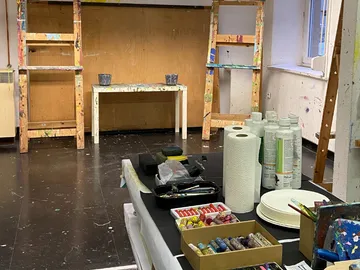 Artistic workshop with paints, brushes and materials scattered around.