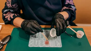 Hands pour resin into flexible forms on a table mat.