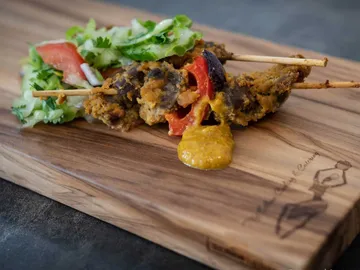 Grilled skewers lie on a wooden board with salad.