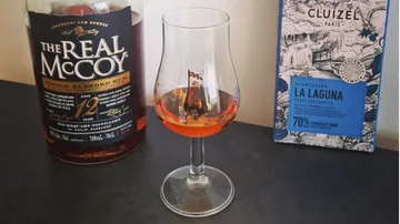 A glass of rum stands next to chocolate and a bottle.