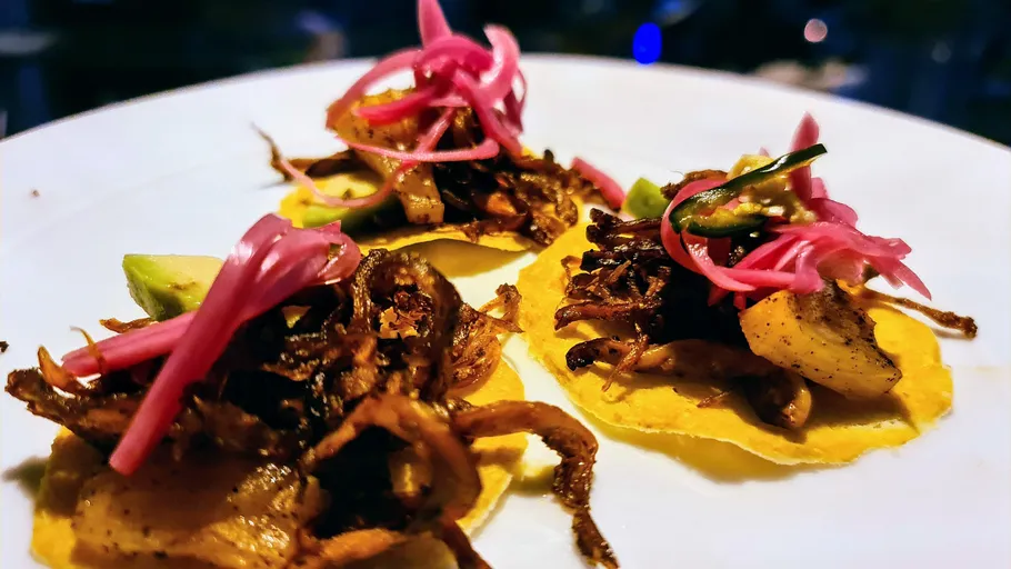 Three tacos with pickled onions and curved meat.