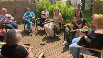 Women sit outdoors and eat from bowls.
