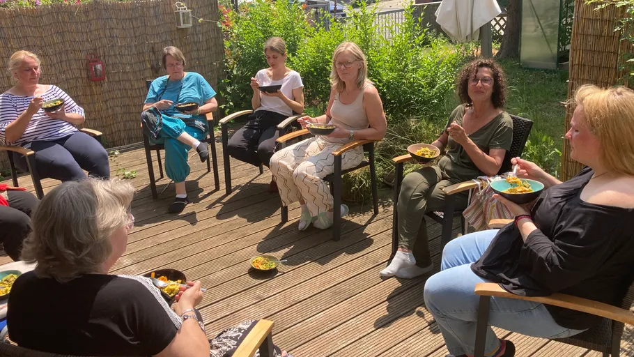 Frauen sitzen im Freien und essen aus Schalen.