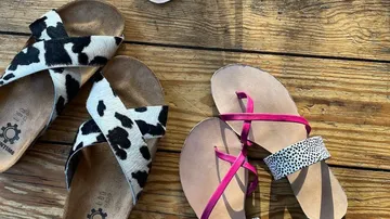 Two pairs of sandals lie on a wooden table.