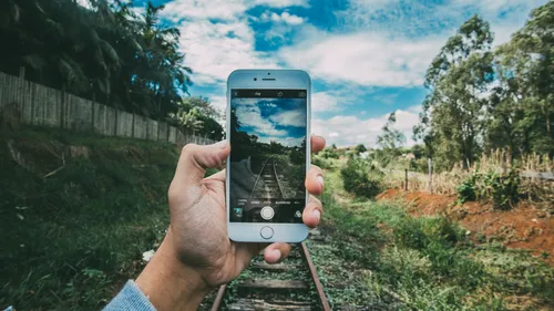 Hand hält Smartphone, das Schienen und Himmel zeigt.