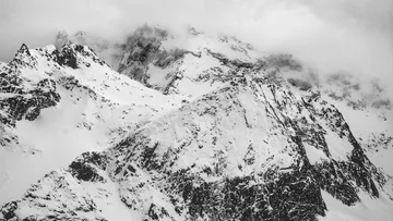 Snow-capped mountains rise up under a cloudy sky.