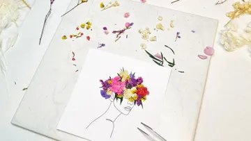 Leaf with a drawn head surrounded by dried flowers.