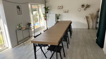 Langer Tisch in hellem Raum mit Pflanzen und Fenstern.