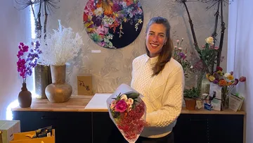 Frau hält Blumenstrauß in blumiger Umgebung, lächelt freundlich.
