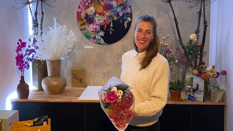Frau hält Blumenstrauß in blumiger Umgebung, lächelt freundlich.