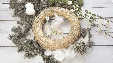 Strohkranz mit Hase, Eiern und Frühlingsblüten dekoriert.