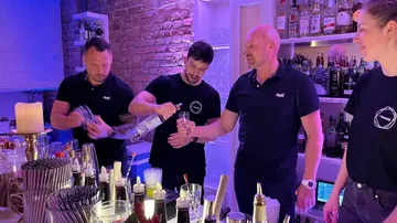 Vier Barkeeper mixen Drinks hinter einer gut bestückten Bar.