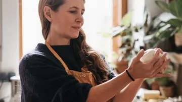 Woman forms dough in a bright, plant-rich kitchen.