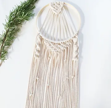 Macrame wall hanger hangs surrounded by green twigs.