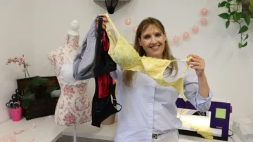 Woman holding three colorful bras in the sewing workshop.
