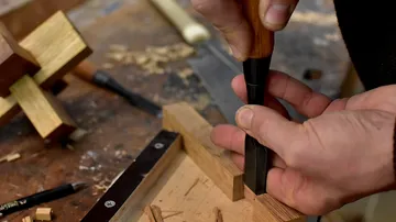 Ein Handwerker bearbeitet Holz mit einem Meißel auf Werkbank.