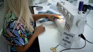 Eine Frau näht an einer Nähmaschine in einem kreativen Raum.