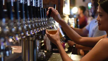 Eine Person zapft Bier an einer Bar mit vielen Zapfhähnen.