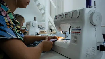 Eine Frau näht an einer Nähmaschine in einem Atelier.