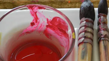 Roter Farbkasten mixen, daneben Pinsel auf einem Tisch.