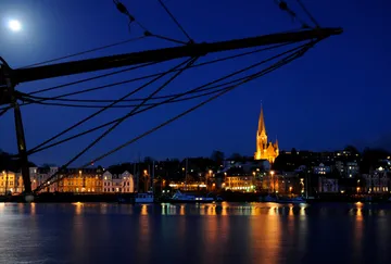 Starry sky, ship mast in front of illuminated waterfront cityscape.
