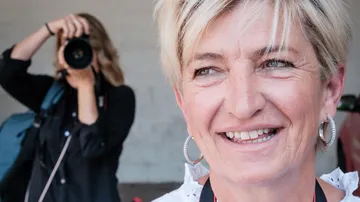 Frau lächelt, während eine andere Person sie fotografiert.