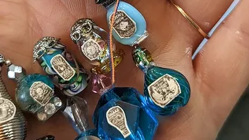 Hand hält farbige Glasperlen mit eingravierten Emblemen.