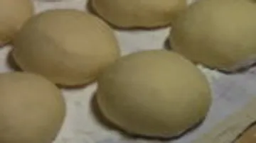 Runde Teigstücke ruhen auf einem Blech in einer Küche.