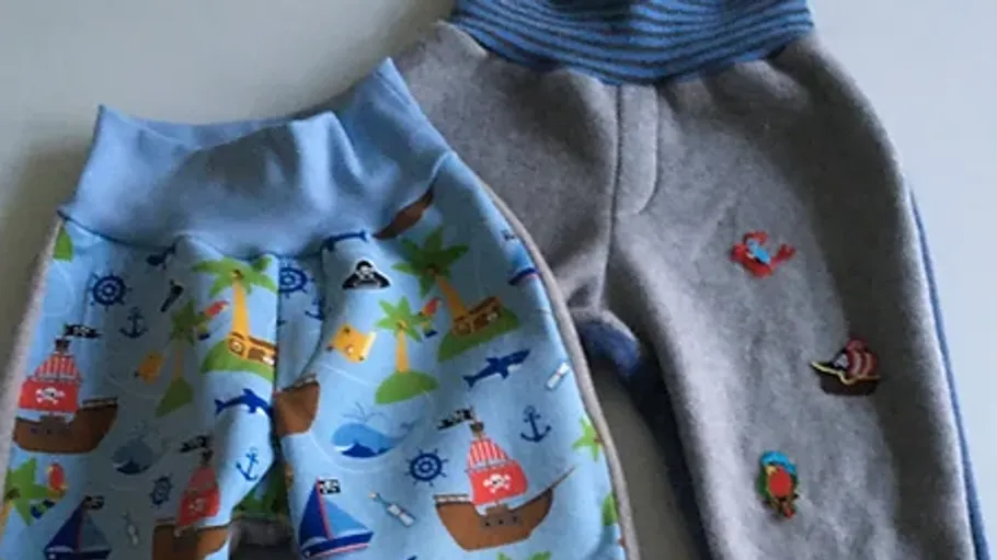 Zwei Kinderhosen, eine bunt mit Piratenschiffen, eine grau mit Stickerei.