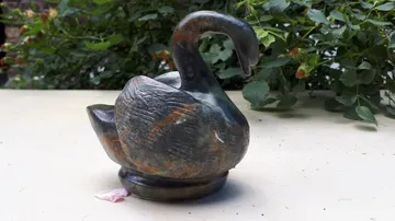 Ein Schwan aus Stein steht auf einem Tisch im Freien.