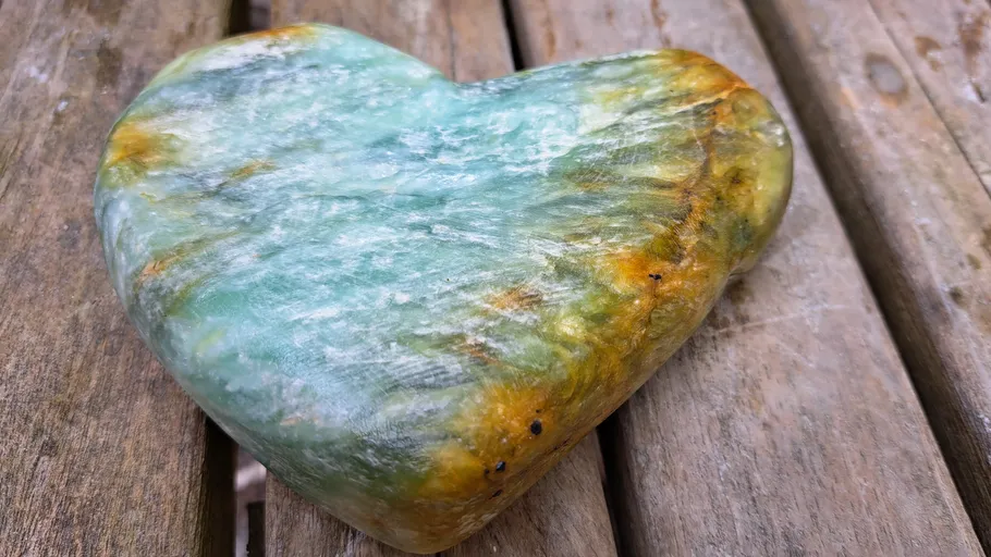 Herzförmiger Stein liegt auf wooden Oberfläche, grünlich gefärbt.