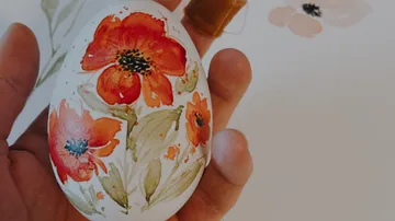 Hand holding painted egg with red floral motifs