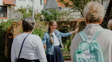 Frau erklärt etwas, während ältere Menschen zuhören, im Freien.