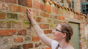 Frau berührt eine Backsteinmauer in einer ruhigen Umgebung.