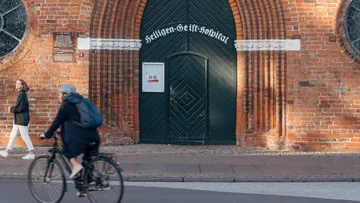Fahrradfahrer fährt vor historischer Backsteinmauer und Eingang.