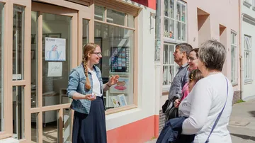 Frau spricht mit Gruppe vor einem Geschäft im Freien.