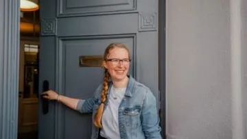 Woman opens a door and smiles friendly.