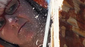 Woman cuts wood, wood chips fly into the air.