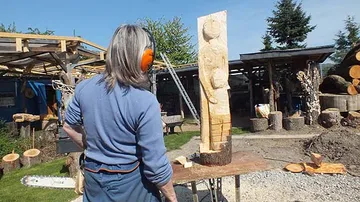 Wood artist works statue with chainsaw outdoors.