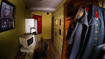 A room with a computer desk, uniform and Soviet flag.