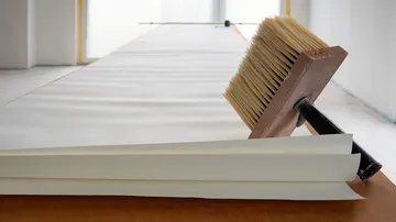 Bürste liegt auf Tapeziertisch und TapetenbahnenTisch, während Papier zum Malen vorbereitet ist.