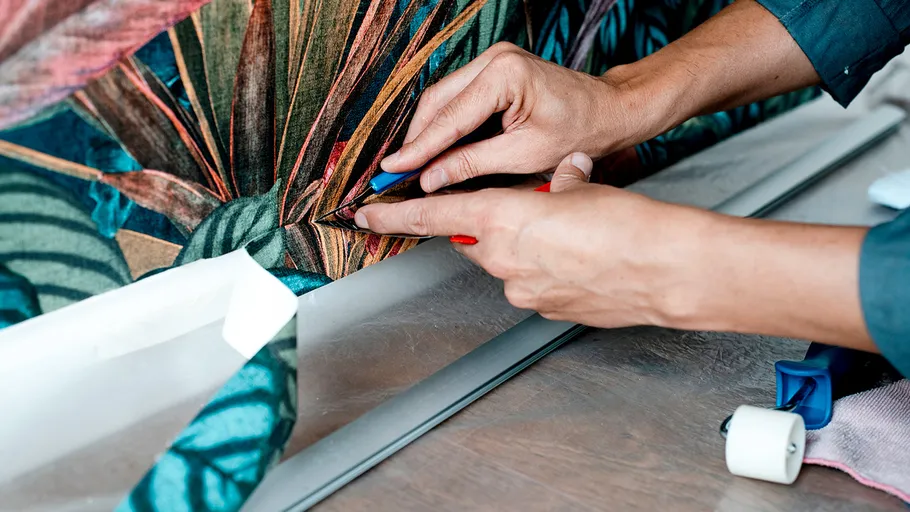 Hands attach wallpaper to a wall with a colorful pattern.