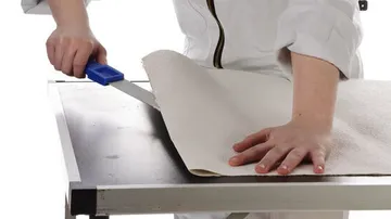 Eine Hand schneidet mit einem Messer eine Tapetenbahn.