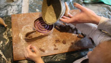 Clay is poured into a mold while hands help.