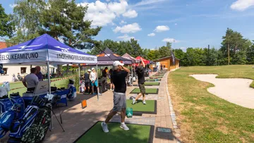 Golfers hit on a driving range in sunny surroundings.