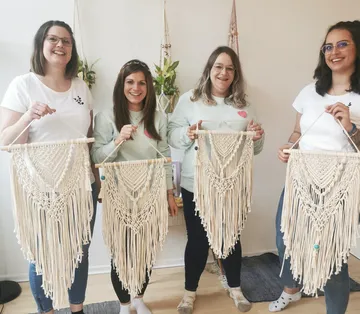 Vier Frauen halten handgeknüpfte Wandbehänge in einem Raum.