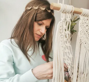 Woman concentrates on macrame artwork in a bright room.