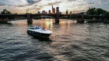 Boat sails on calm water at sunset, city in the background.