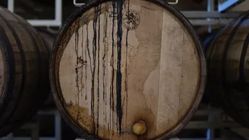 A wooden barrel that loses liquid is in a warehouse.